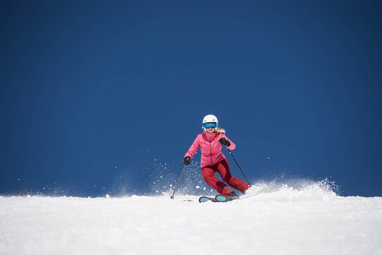 A person in pink ski gear skiing down the slope under a sunny blue sky.