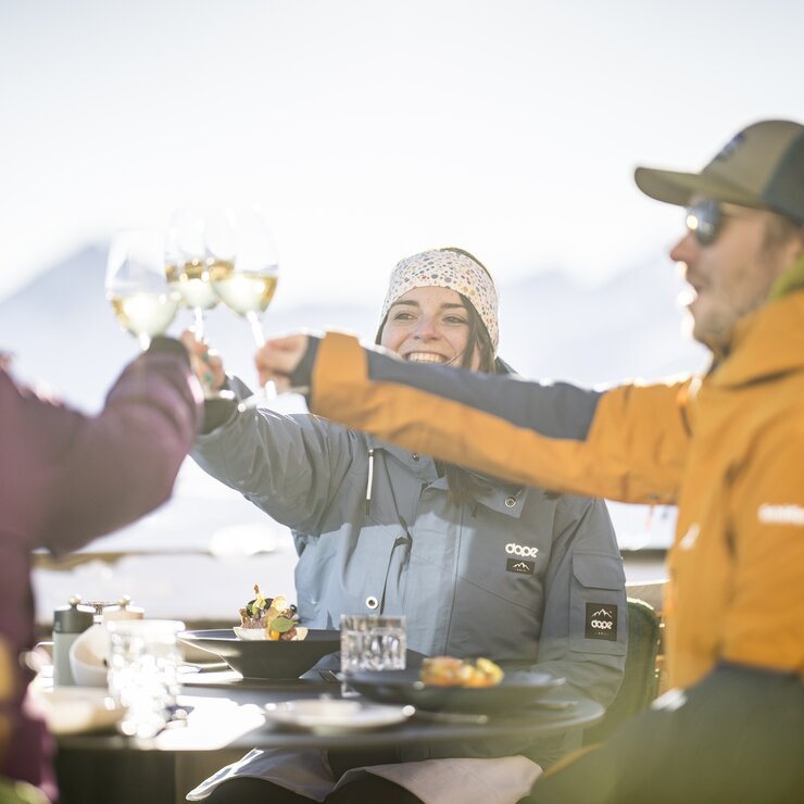 Group toasting with drinks on alpine terrace during spring skiing.