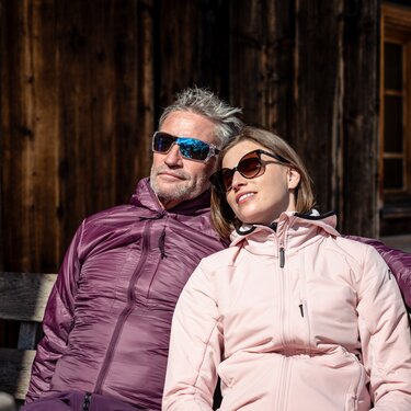 A couple relaxing on a wooden bench during spring skiing.
