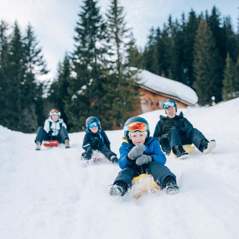Four people sledding down a snowy hill together.