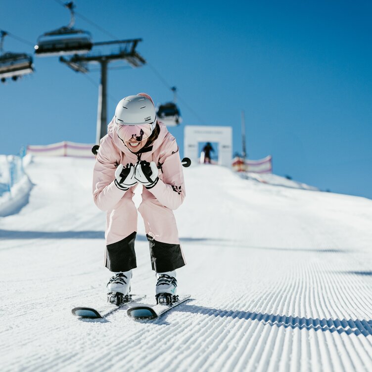 Woman in pink ski jacket skiing downhill. Ski lift in the background.