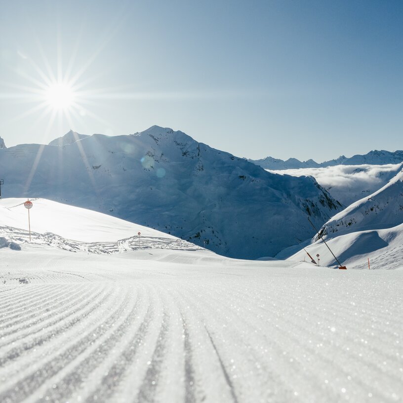 Sonniger Skitag auf einer frisch präparierten Piste in den Bergen.