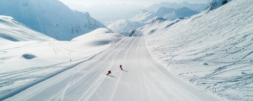 Two skiers descending a wide, snow-covered slope.