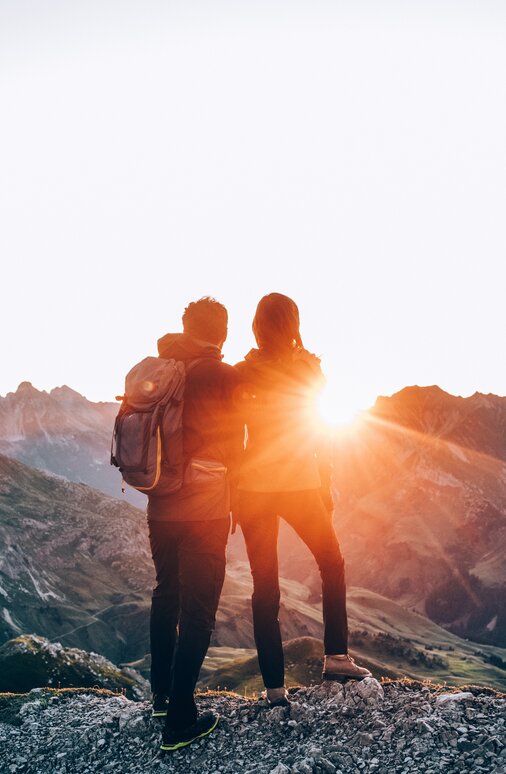 Two people standing on a mountain watching the sunrise.