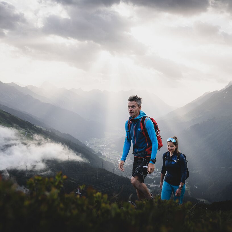 Two hikers in the mountains with sun rays and clouds.
