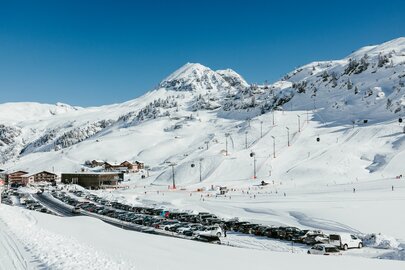 Verschneite Berglandschaft mit Skilift und geparkten Autos.