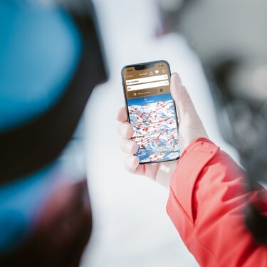 Skifahrer in roter Jacke öffnet den Pistenplan von Ski Arlberg auf seinem Smartphone.
