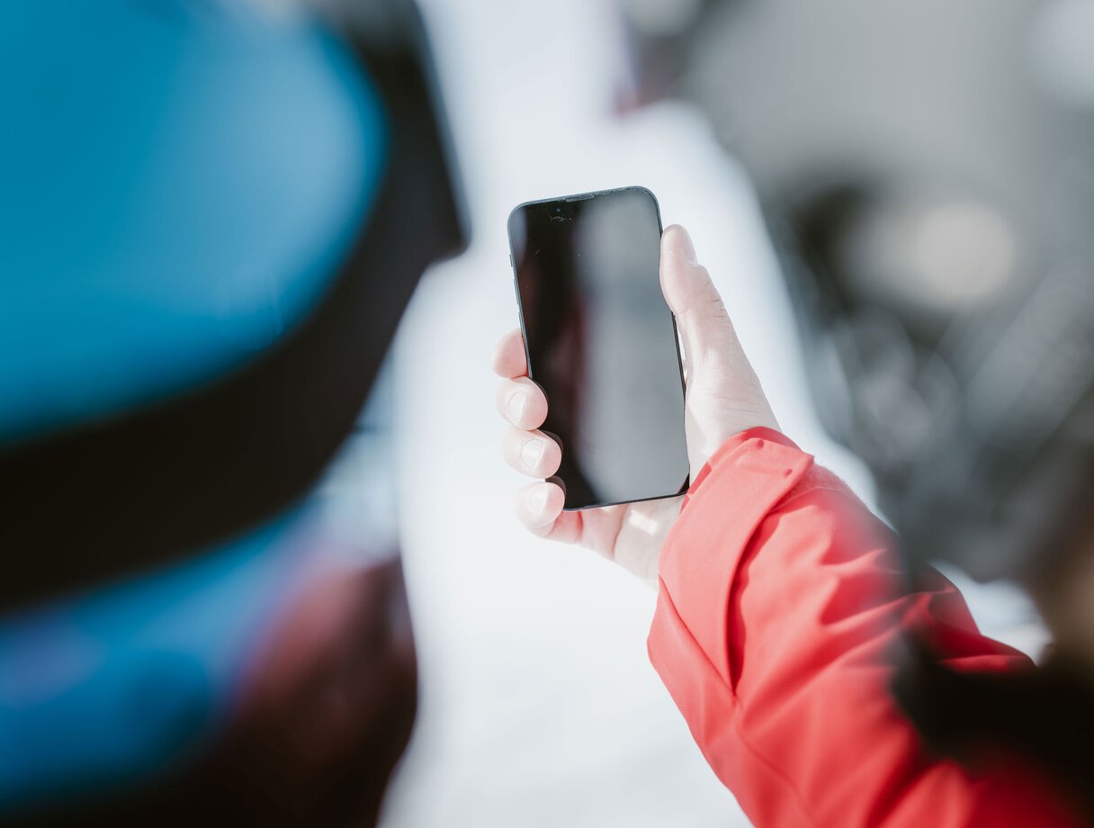 Person in roter Jacke hält Smartphone, Bildschirm aus.