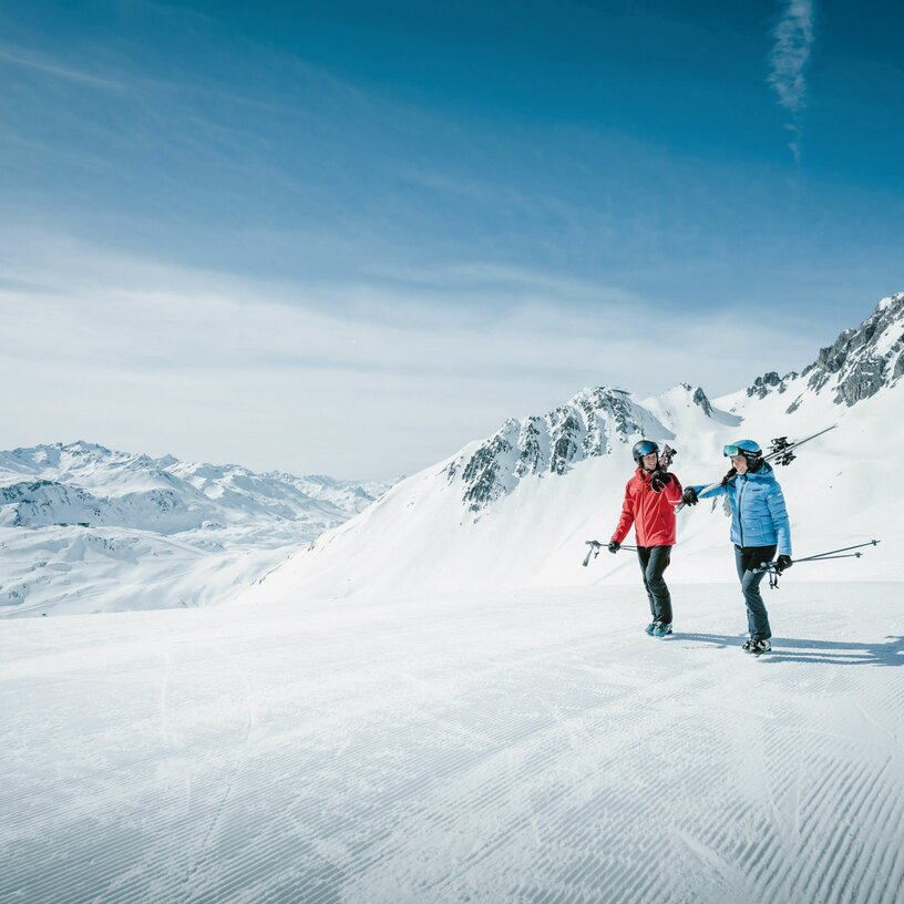 Two people with ski gear on a snowy mountain landscape.