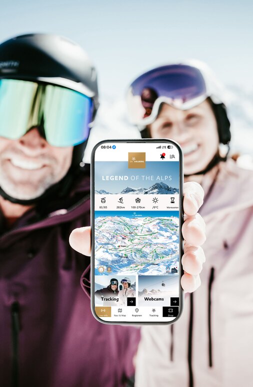 Ski couple showing mobile app in sunny mountain landscape.