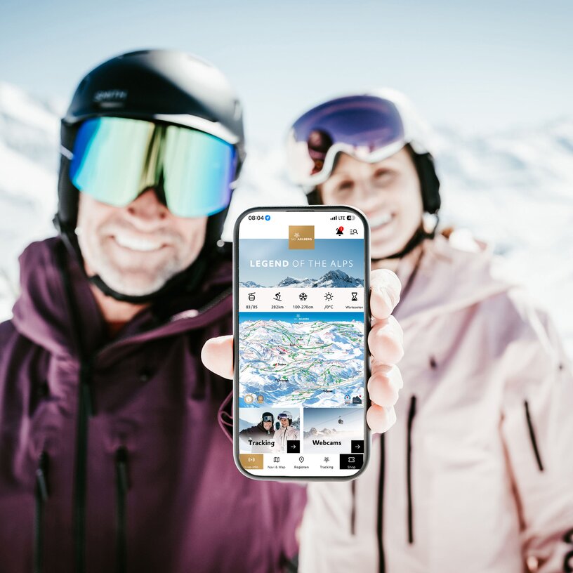 Ski couple showing mobile app in sunny mountain landscape.