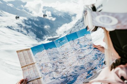 Person studiert Karte der Skiregion Ski Arlberg vor einer schneebedeckten Berglandschaft.