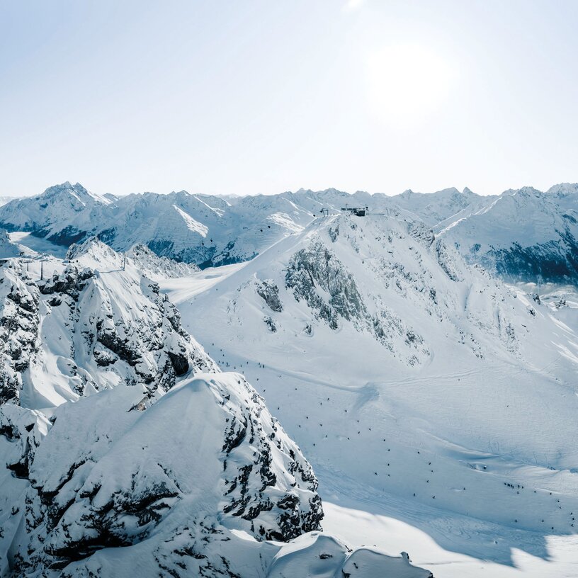 Verschneite Berge mit Skipisten unter strahlendem Sonnenschein.
