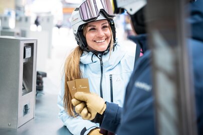 Frau in Skibekleidung lächelt mit Skipass am Schalter.