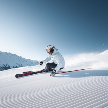 Person fährt schwungvoll auf präparierter Skipiste bei Sonnenschein.