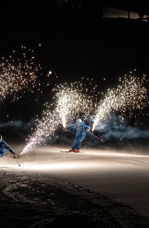 Two skiers at night holding sparking flares.