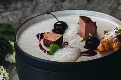 Modernes Gericht mit Wildpastete, Kirschen und ansprechender Garnitur.