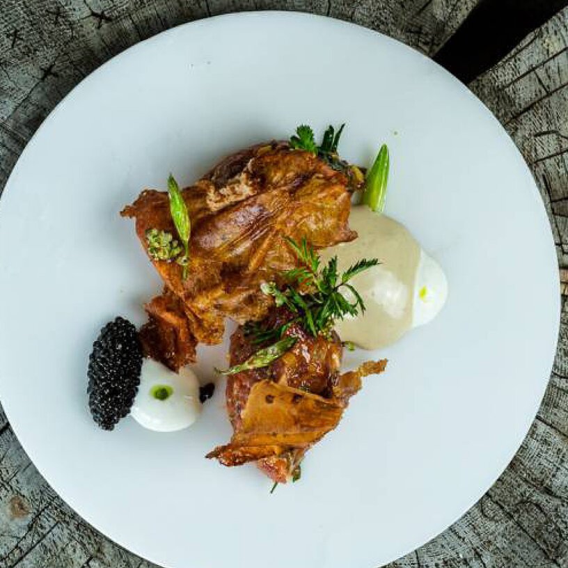 Ein kunstvoll angerichtetes Gericht auf einem weißen Teller, serviert auf einem rustikalen Holztisch.