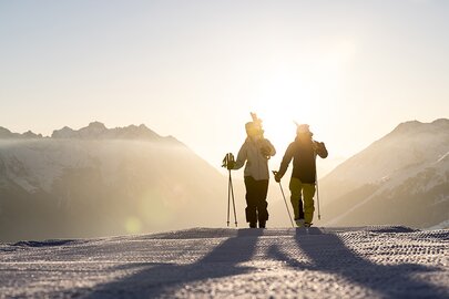 Zwei Personen auf einer Skipiste mit Skiern, bei Sonnenuntergang.