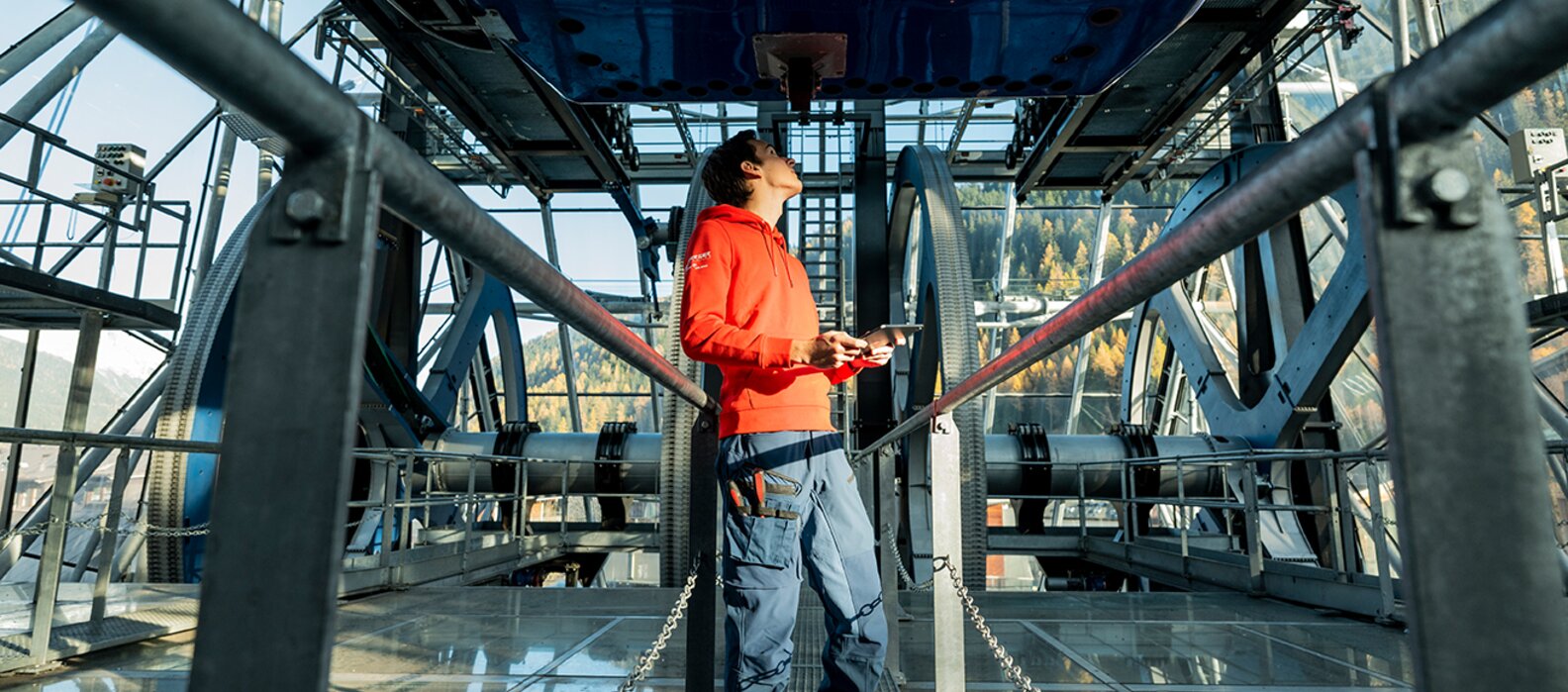 Mann im roten Pullover überprüft Mechanik in Seilbahnstation.