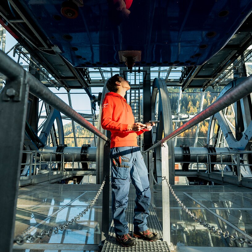 Mann im roten Pullover überprüft Mechanik in Seilbahnstation.