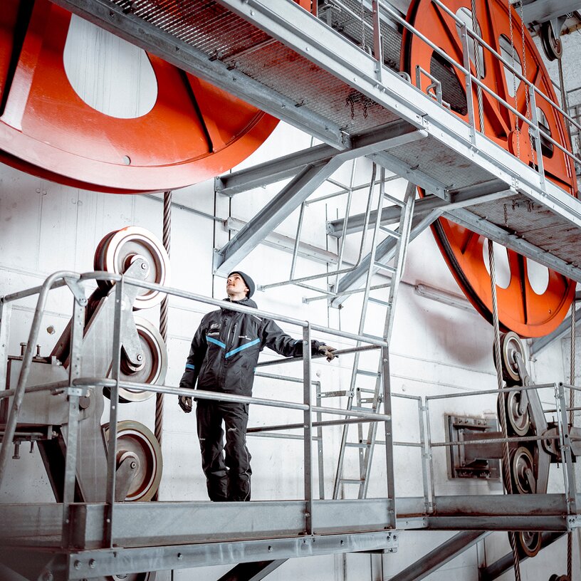 Ein Techniker steht auf einer Plattform und inspiziert große Maschinenräder in einer Halle.