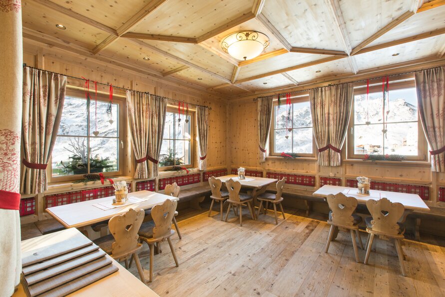 Wood-paneled room with table sets and decorative curtains, view of snowy landscape.
