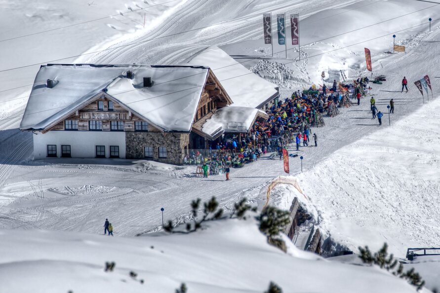 Crowd in front of a ski restaurant in the snow, many skiers visible.
