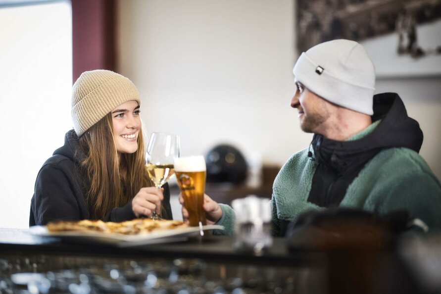 Two people clinking drinks and enjoying pizza.