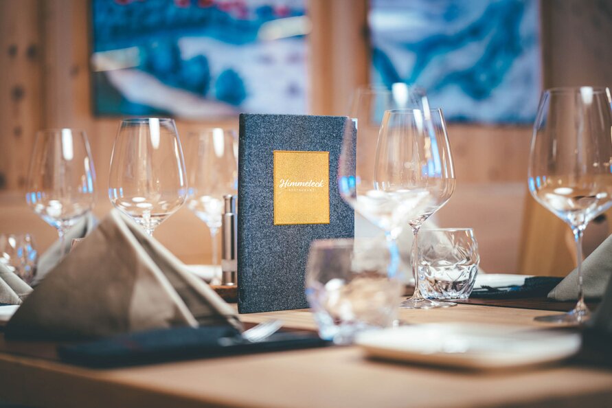 Neatly set table at Restaurant Himmeleck with menu and wine glasses.