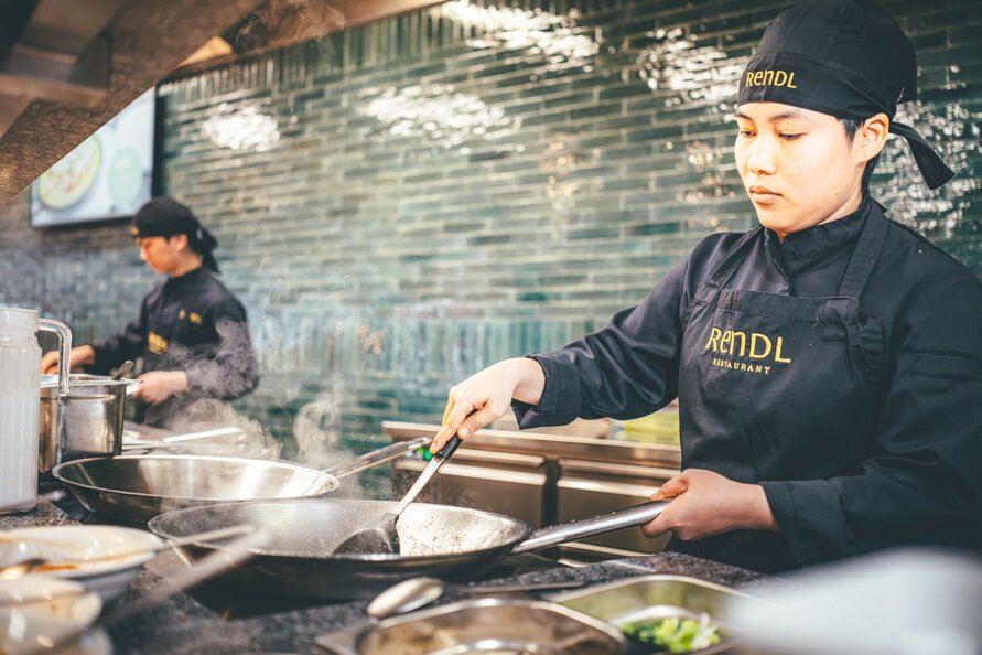 Ein Koch brät in der Küche des Rendl Restaurants Speisen in einer Pfanne an.