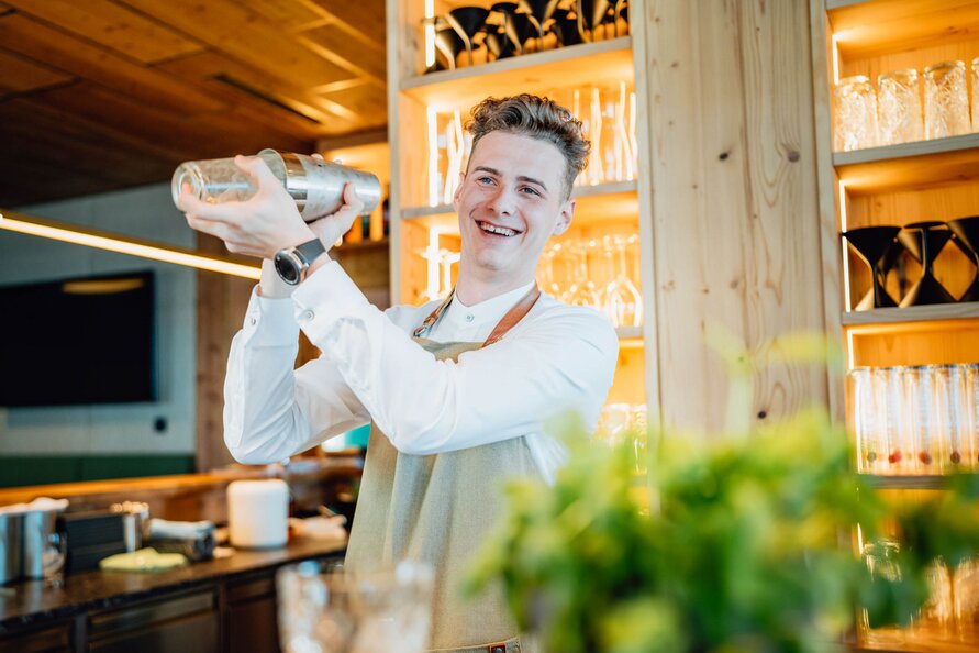 A bartender at Verwallstube shaking a cocktail mixer and smiling cheerfully.