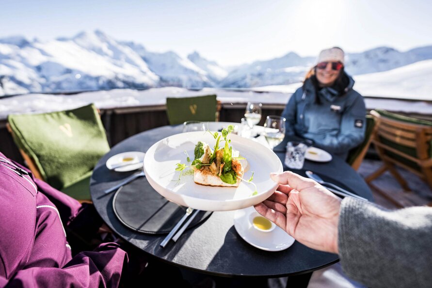 Alpine panorama with guests dining on the terrace at Restaurant Verwallstube enjoying gourmet food. 