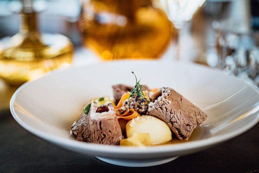 A plate of braised veal with potatoes and vegetables at Restaurant Verwallstube, presented in an elegant setting. 