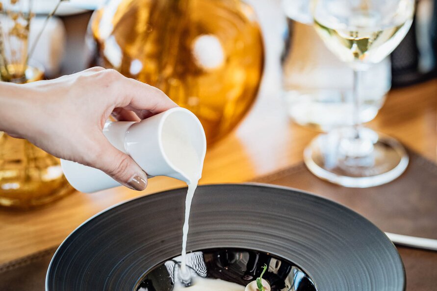 Hand pouring soup into a bowl with mushrooms at Restaurant Himmeleck.
