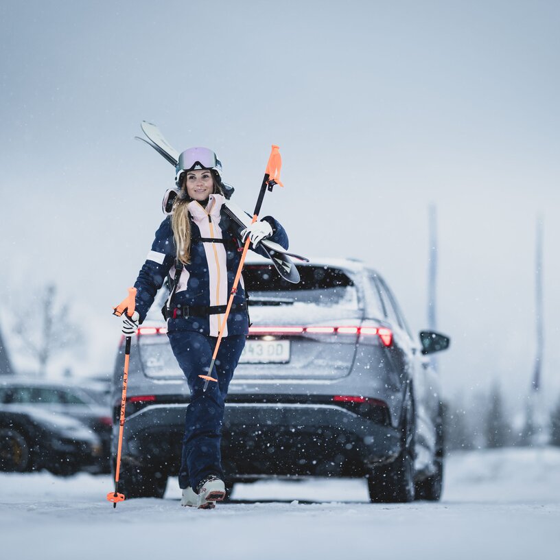 Person in ski gear standing in front of a car, ready to ski.