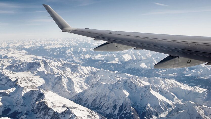 View from airplane of snow-covered mountain ranges from high altitude.