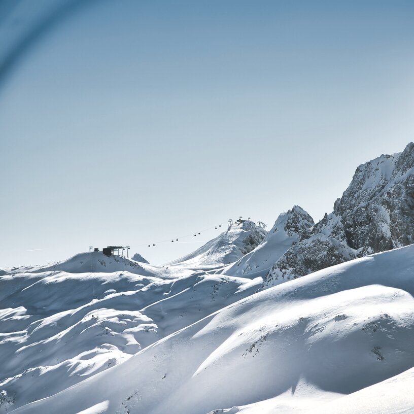 Malerisches Bild von schneebedeckten Bergen unter klarem Himmel mit einem Skilift am Horizont.