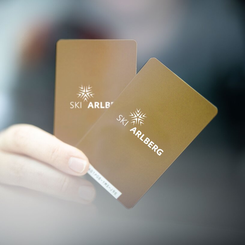 Hand holding two golden Ski Arlberg ski passes.