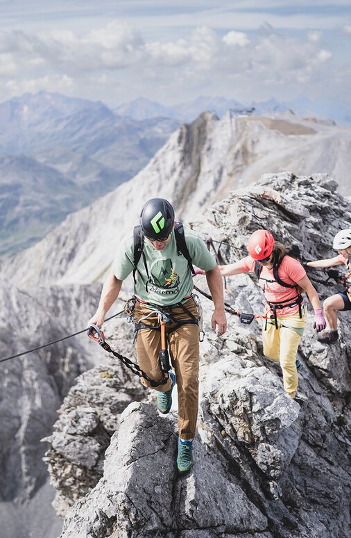 Eine Gruppe von Kletterern mit Sicherheitsausrüstung auf einem schmalen Berggrat.