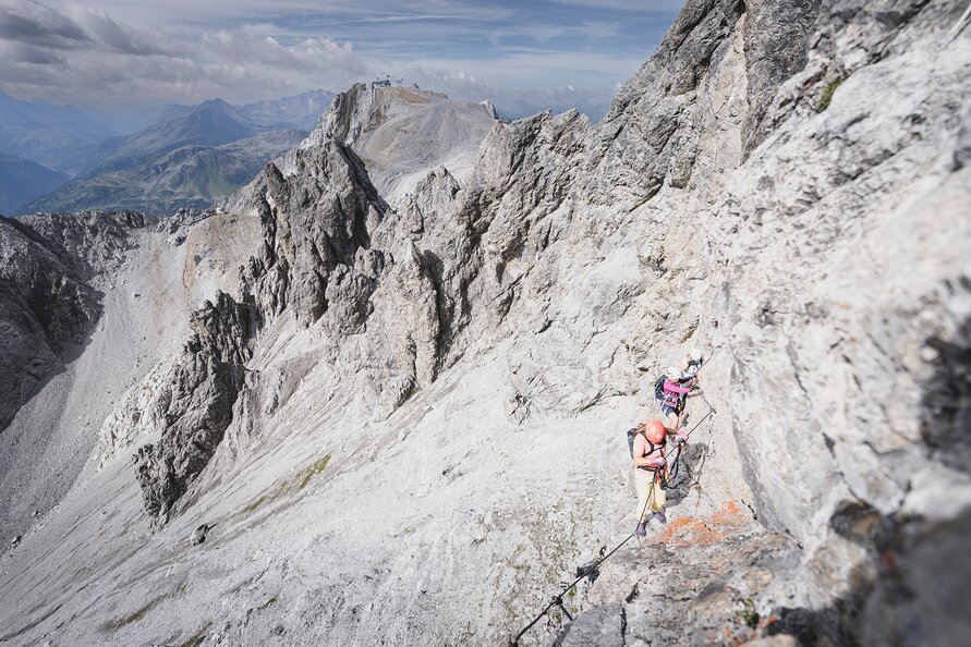 Two climbers securing themselves with a rope on a steep mountain path.