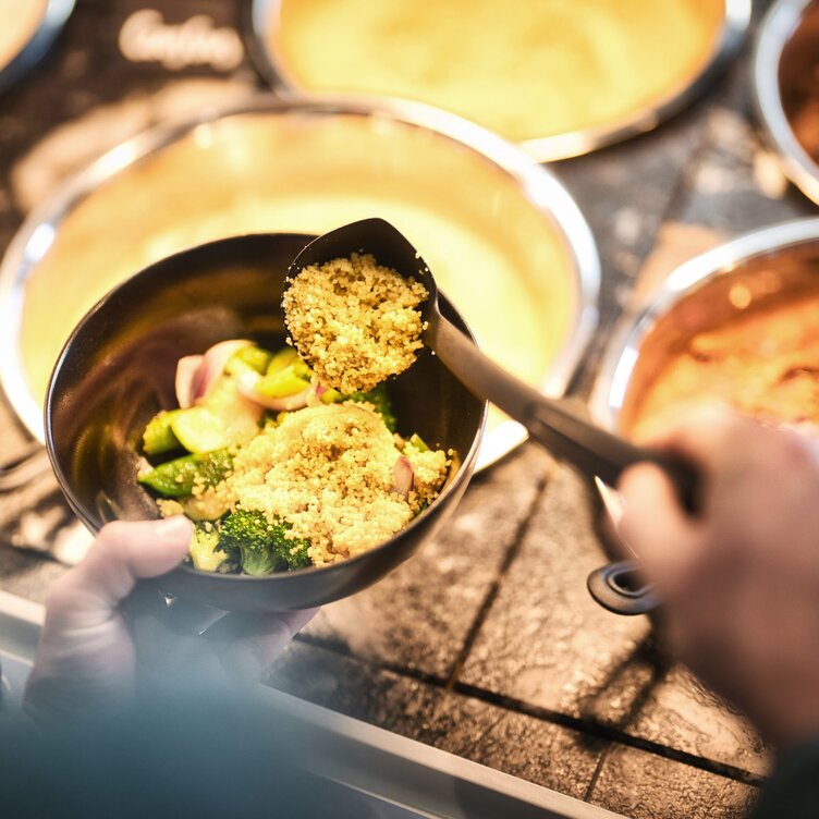 Eine Person bedient sich am Buffet und nimmt sich Gemüse mit Couscous.