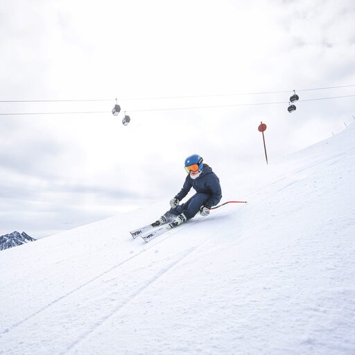 Skifahrer in voller Fahrt auf schneebedecktem Hang unter der Seilbahn.