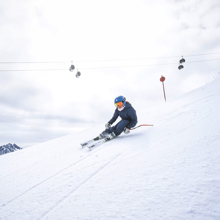 Skier speeding down snowy slope under cable cars.