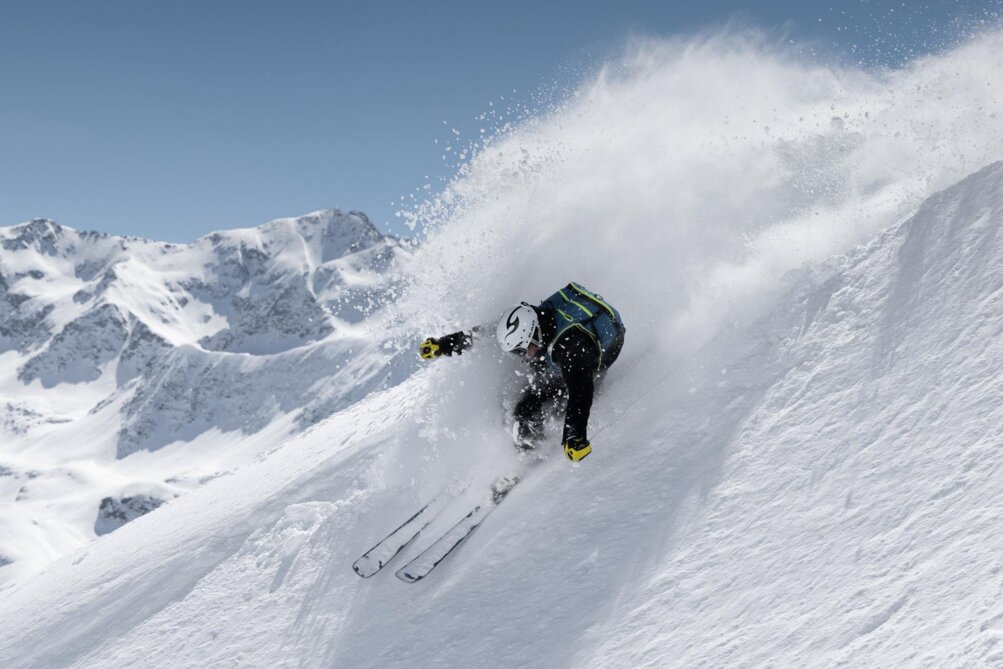 A skier in action on a steep snowy slope against a mountain backdrop.
