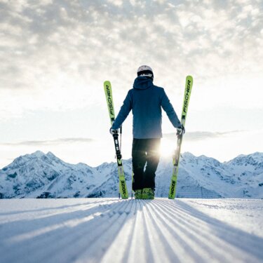 A person with skis in front of a picturesque mountain landscape in sunlight.