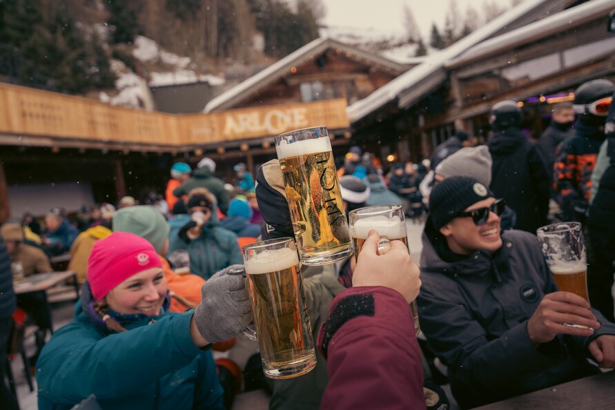 Group of people celebrating with beer mugs outdoors in snowy setting.