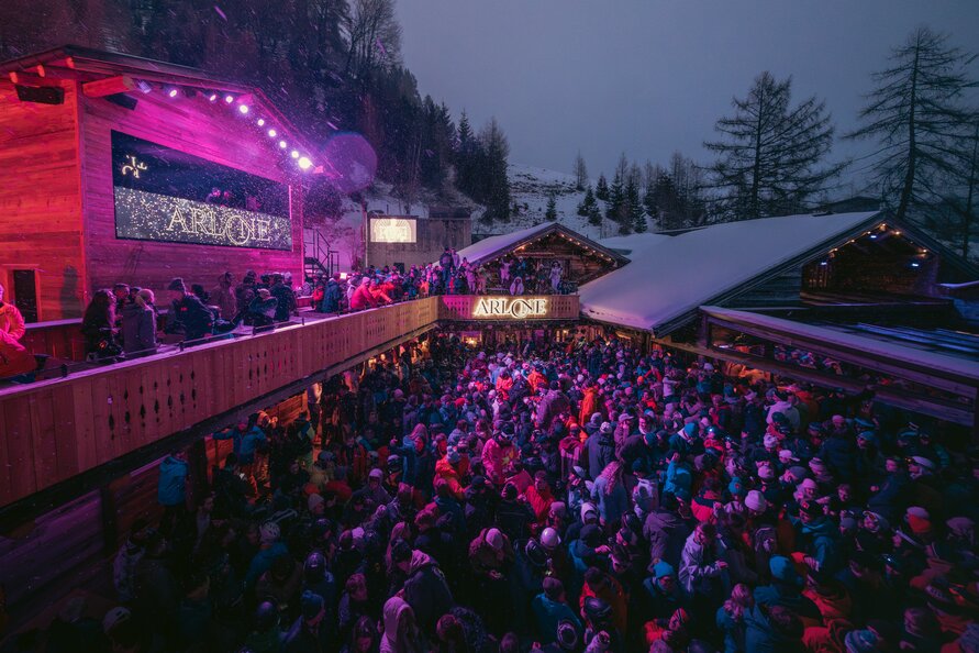 Large crowd enjoying an outdoor nighttime party with stage and lighting.