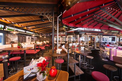 Innenansicht einer rustikalen Bar mit vielen Sitzplätzen, Holztischen und einer einladenden Atmosphäre.