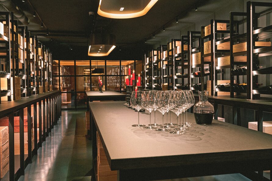 Wine cellar with long tables, wine glasses, and shelves full of wine bottles.